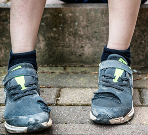 Unkenntliches Kind sitzt mit kaputten Schuhen auf Gehweg